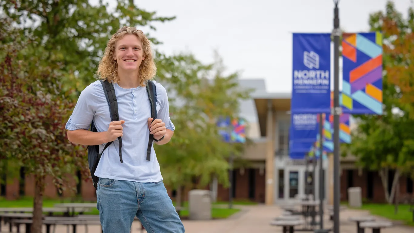 male student smiling on campus with nhcc banners in the background