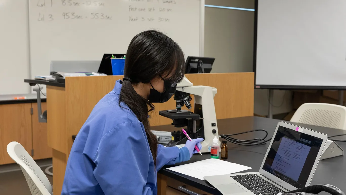 student sitting at table with microscope and laptop