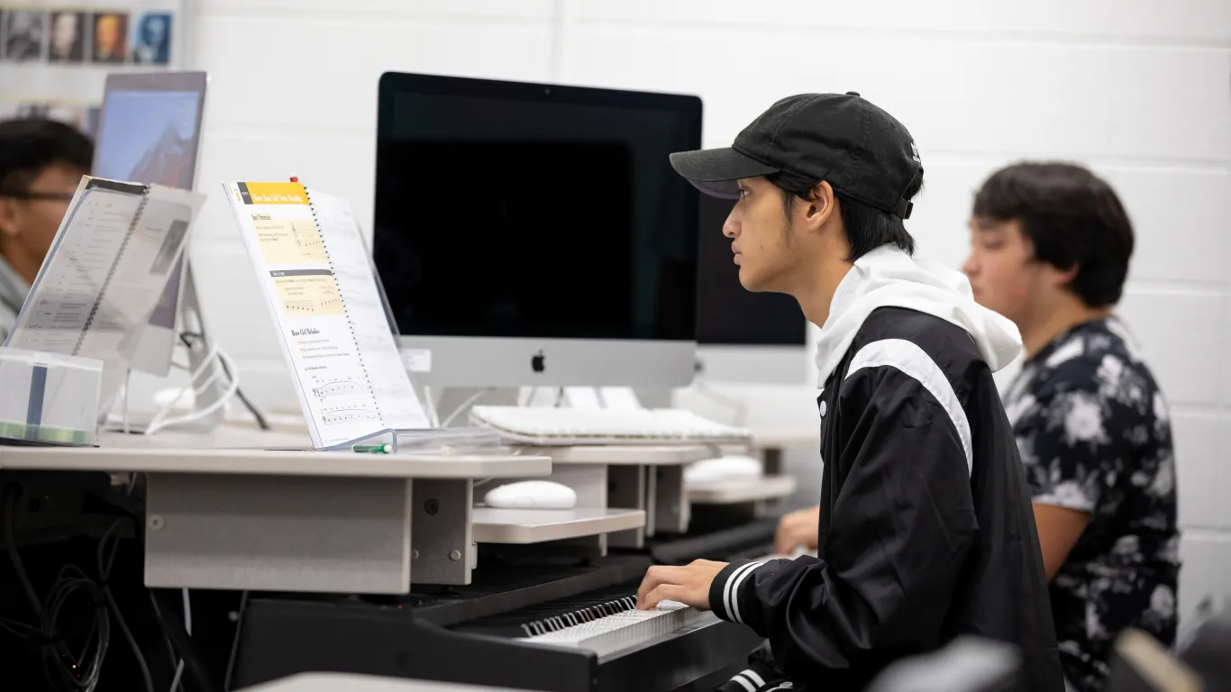 students in a classroom working at desks with pianos