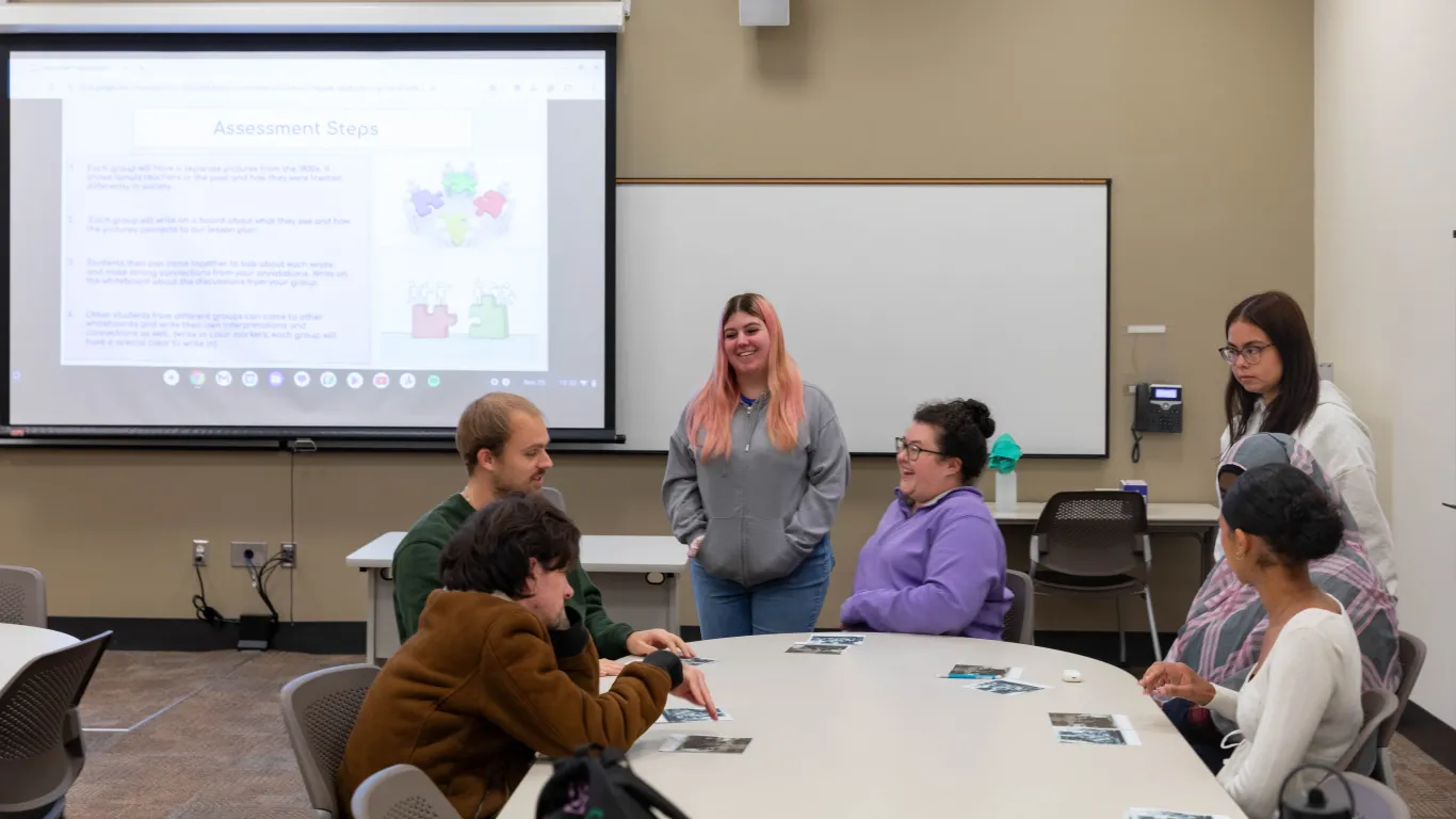 students talking at table while another student is presenting