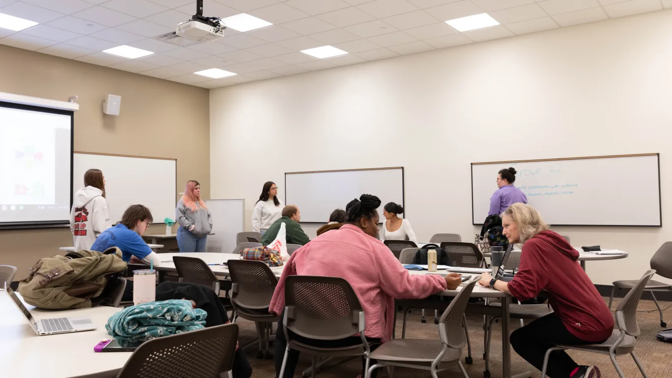 a student talking to an instructor in a classroom while other students do an activity 