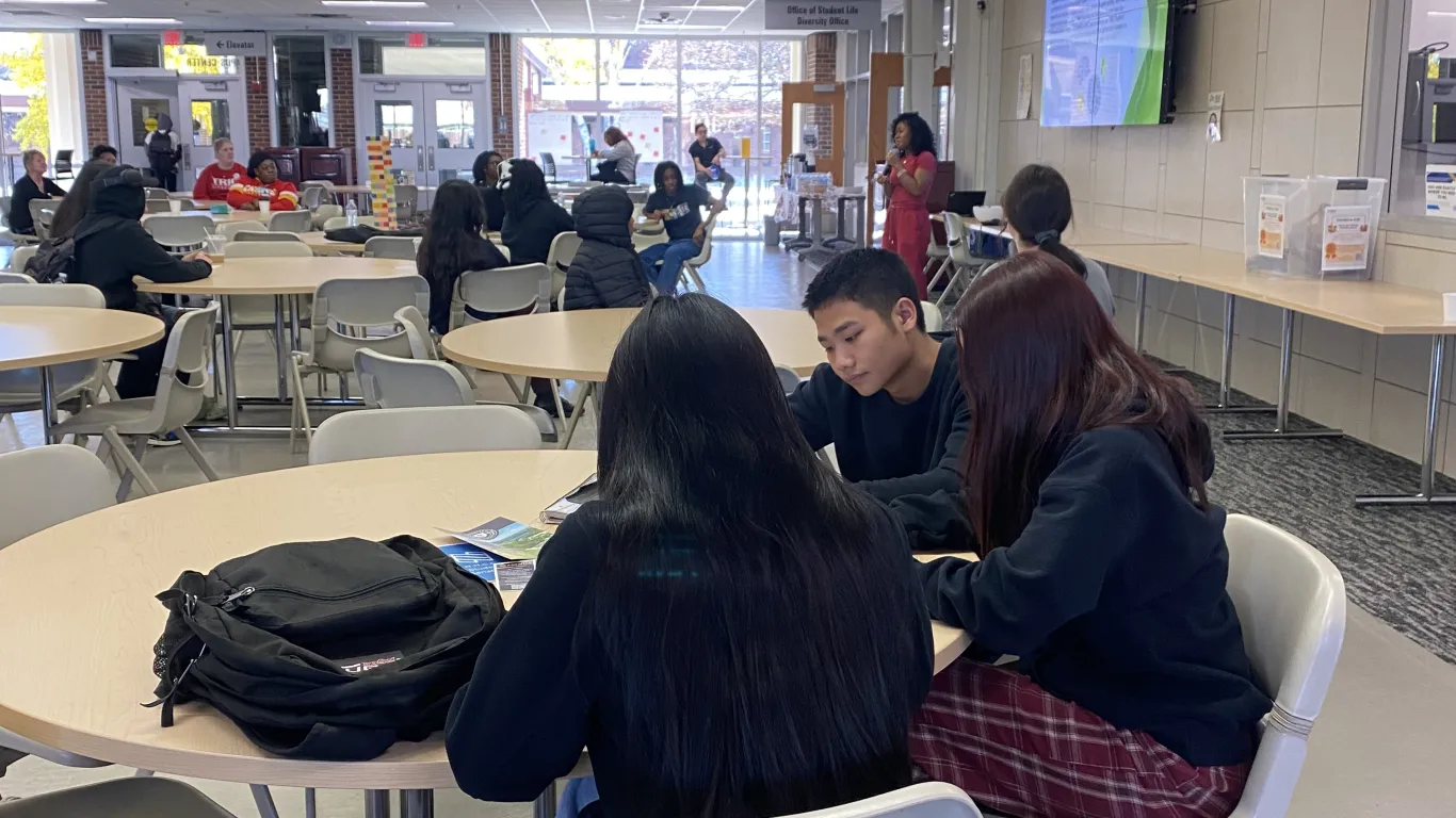 a photo of a student standing at the front of a room talking into a microphone, sharing her story with a room of people. 