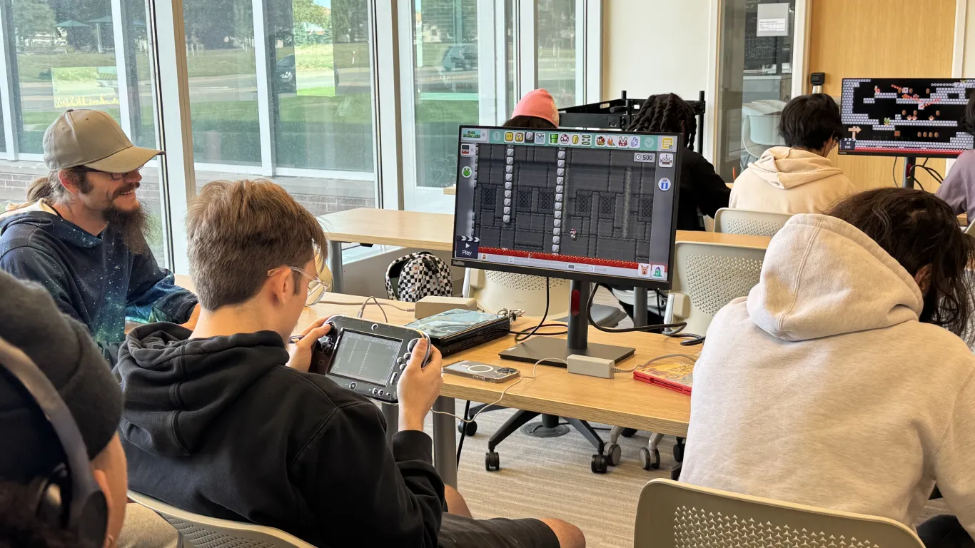 students in classroom working laptops by a window