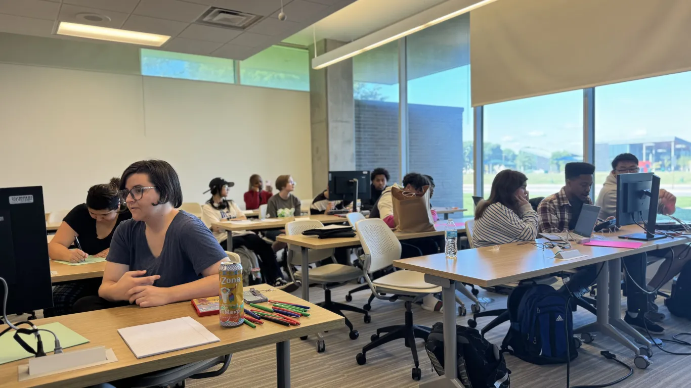 students in a classroom talking and looking at computers