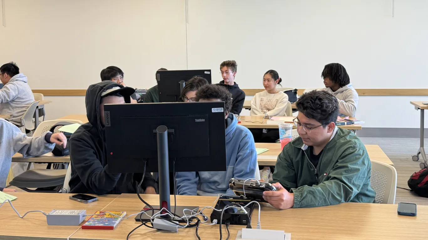 students holding an external computer drive near a monitor