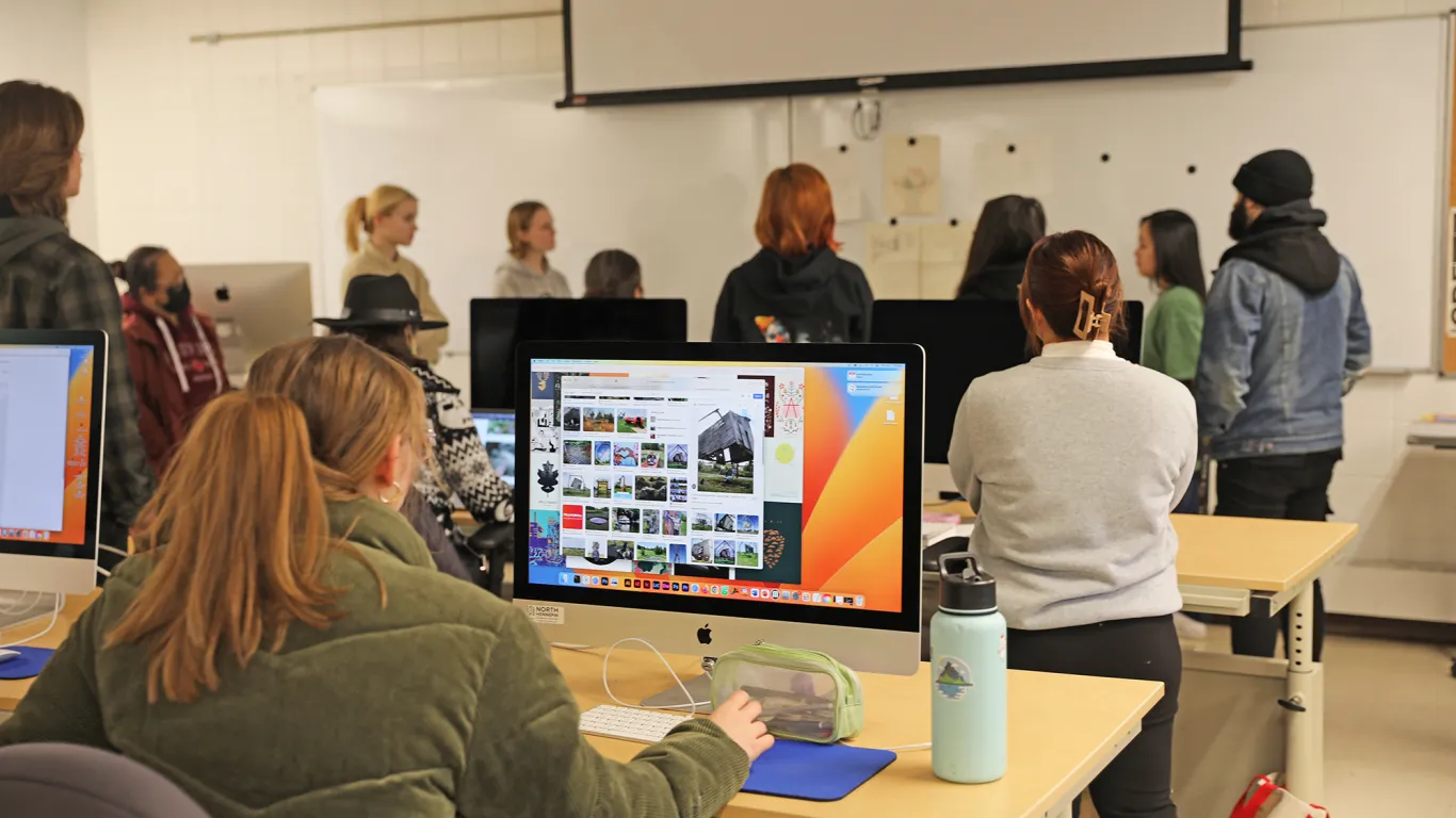 one student at a desk with a computer with students in the background