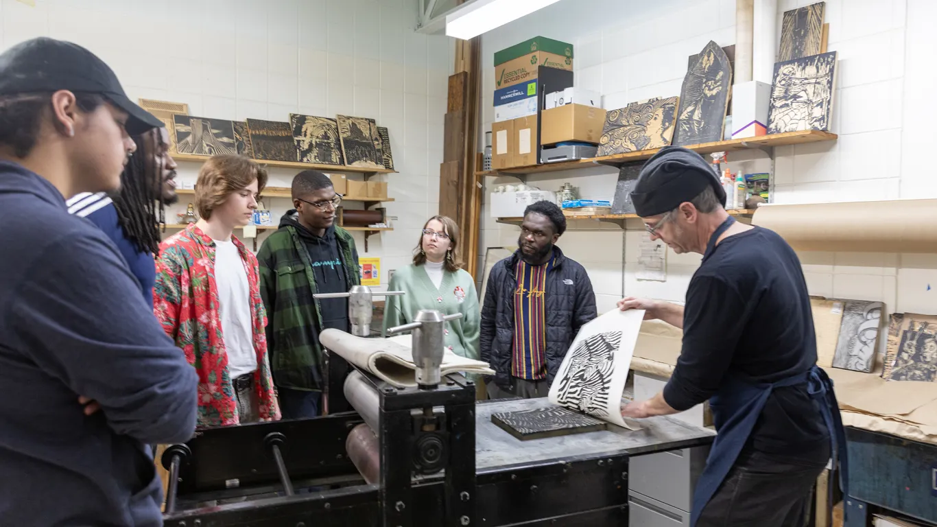 an instructor lifting a print from a press while students watch