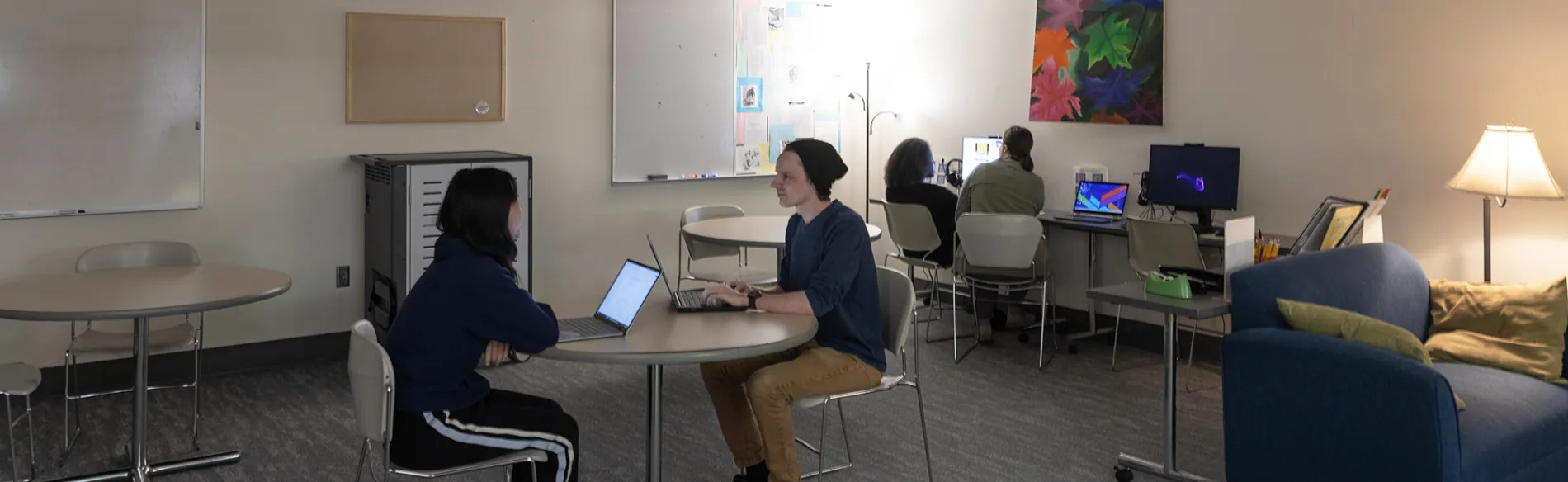 students at a table in a large room with another student working in the background