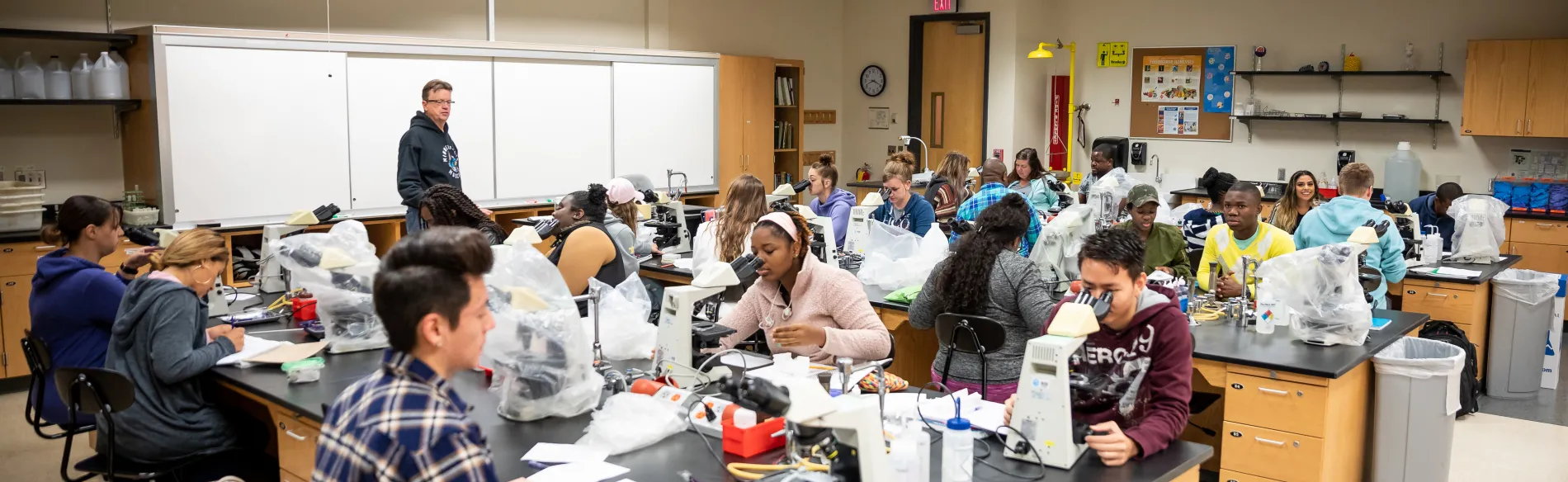 students working on microscopes in a large classroom 