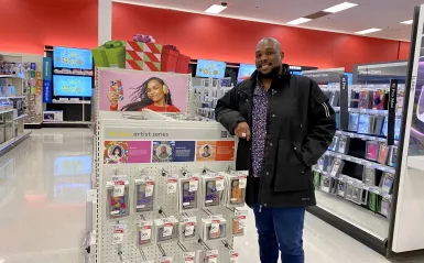 a photo of NHCC graduate, Ameen Taahir, standing next to a display at Target featuring his product designs