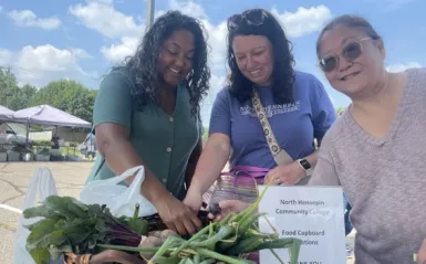 a photo of three NHCC staff members smiling while picking out produce at the Brooklyn Park Farmers Market 