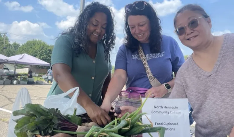 a photo of three NHCC staff members smiling while picking out produce at the Brooklyn Park Farmers Market 