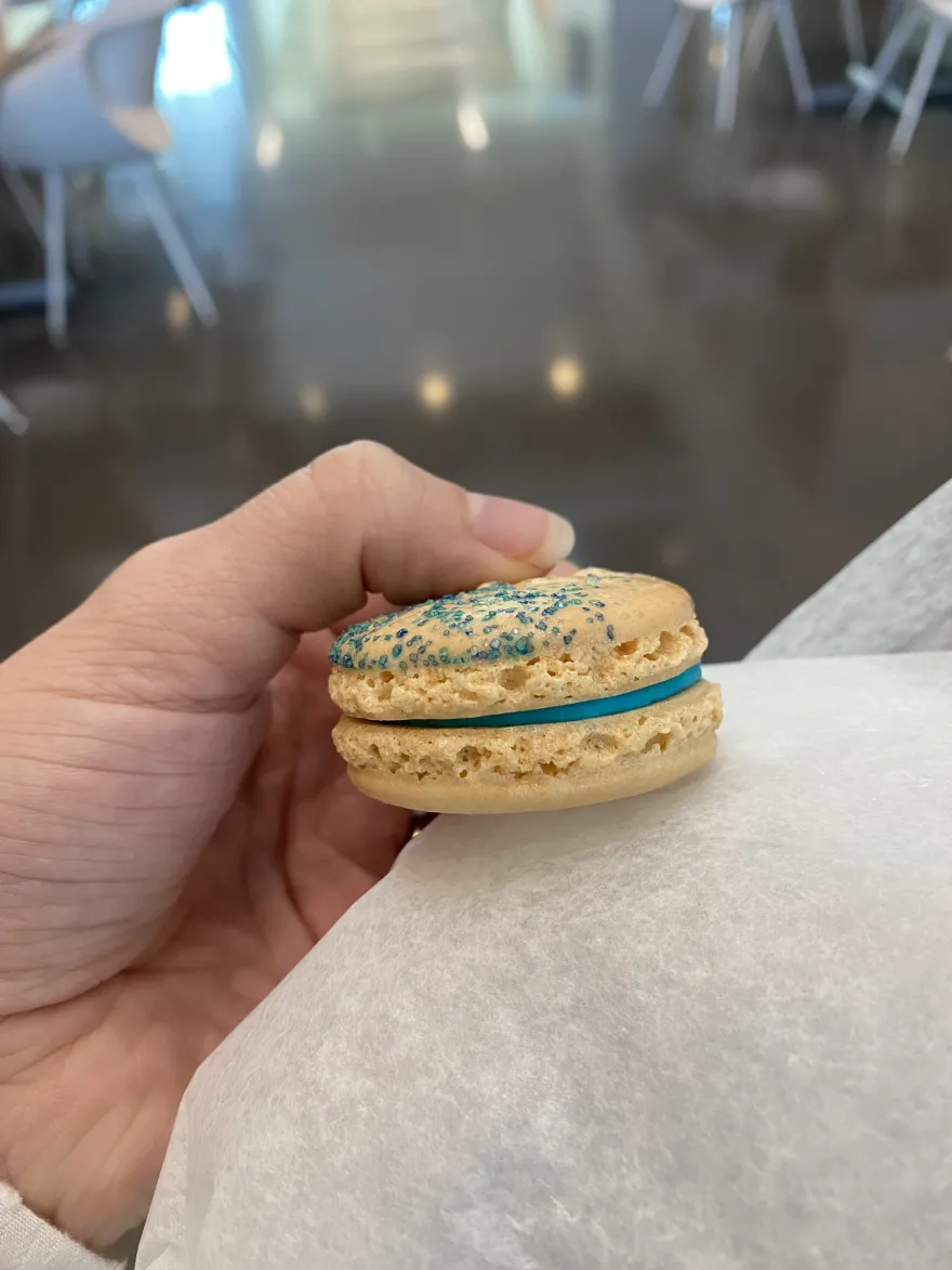 a photo of a white, marshmallow flavored macaron with blue frosting in the center and blue sprinkles on top