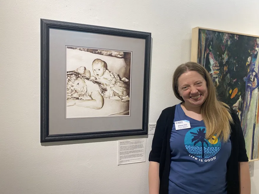 a photo of NHCC alumni, Brittany Kiser smiling next to her painting