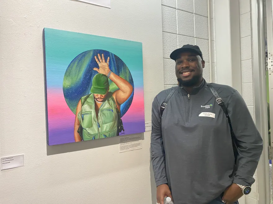 a photo of NHCC alum, Amen Taahir smiling next to his painting