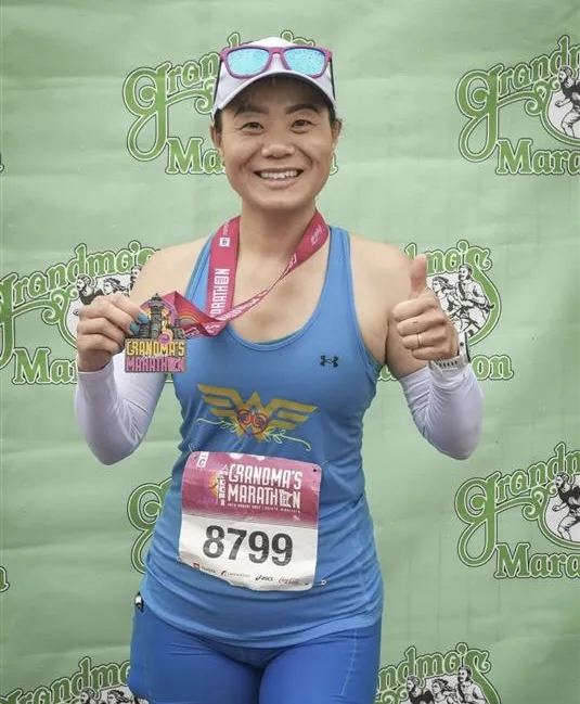 a photo of NHCC academic advisor, Anong Thor, after running the Grandma's Marathon, smiling with her medal in Duluth, MN. 