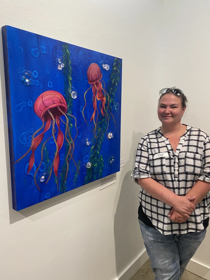 a photo of NHCC alumni, Jess Forga, standing next to her painting