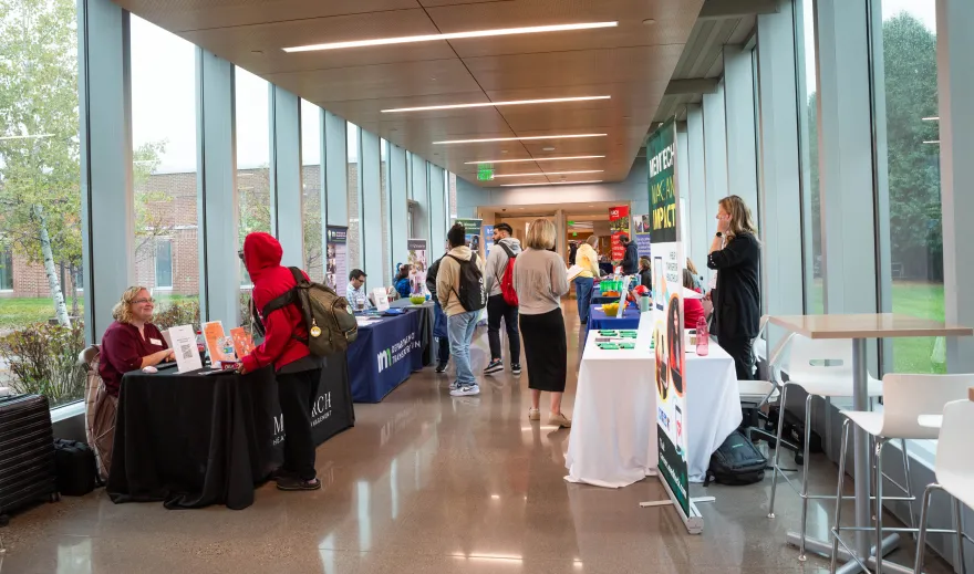 a photo in NHCC's BHCC hallway of STEM career tables and guest staff speaking to students as they walk by. 