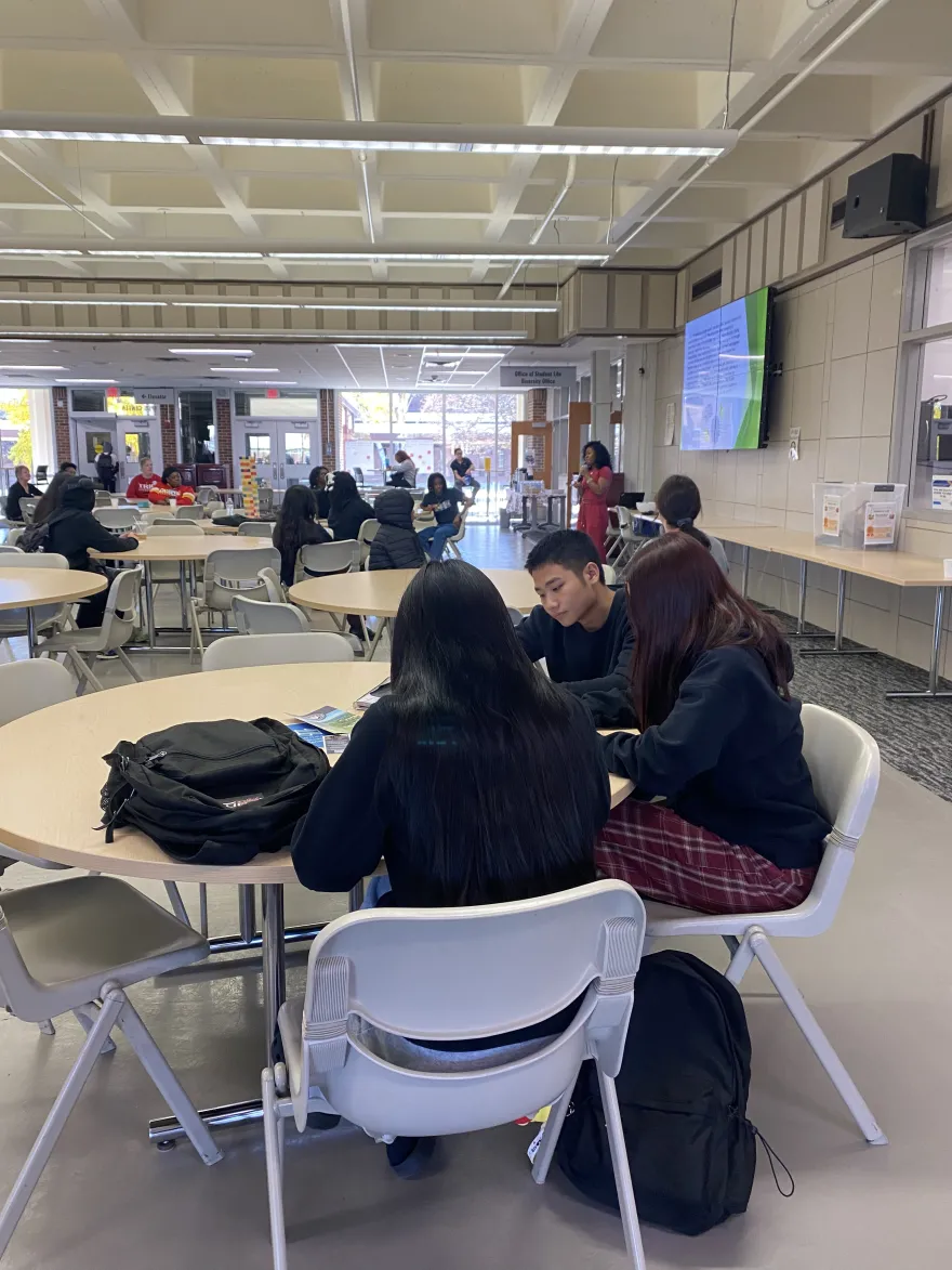 a photo of a student standing at the front of a room talking into a microphone, sharing her story with a room of people. 