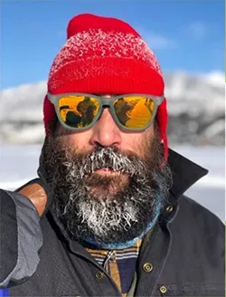 man with beard in an outdoor frigid environment wearing a red hat