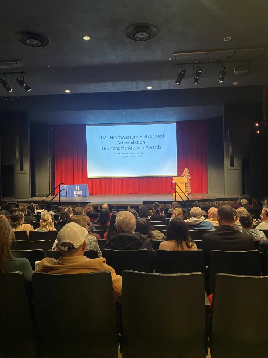 a photo of NHCC dean, Gretchen speaking to an audience in the theatre for the High School Art Show Awards Reception. 