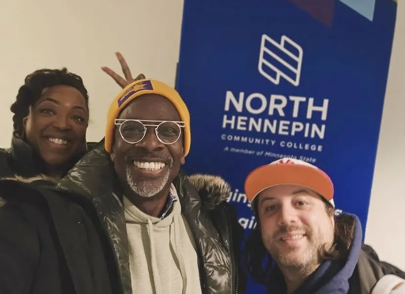 this is a photo of two staff members from On Stage Theatre smiling next to an NHCC sign with special guest, Harry Waters Jr. 