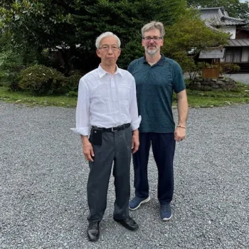 two men standing on a road with trees in the background